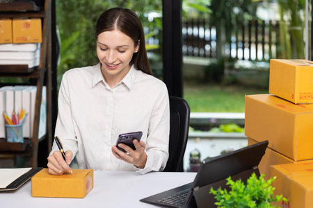 Business owner writing customer address on parcel boxes to deliver products to customers at home. Woman writing address on cardboard box at workplace. Small business entrepreneur SME.の写真素材