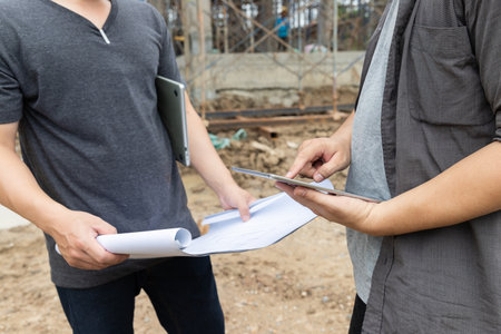 Team of construction workers discussing project details with blueprint in construction site.の写真素材