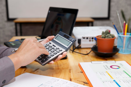 A professional hand calculating numbers with a calculator, pen in hand, while a laptop rest nearby, highlighting focus and precision in financial work.の写真素材