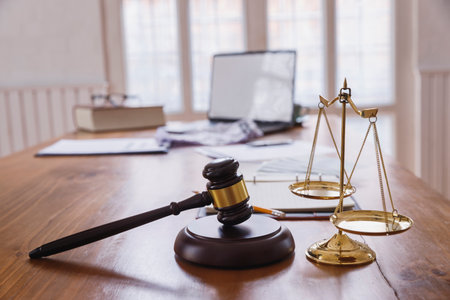 A gavel and scales of justice on a wooden desk symbolize the balance and authority of the legal system. Legal documents and a laptop reflect the modern integration of technology in law.の写真素材