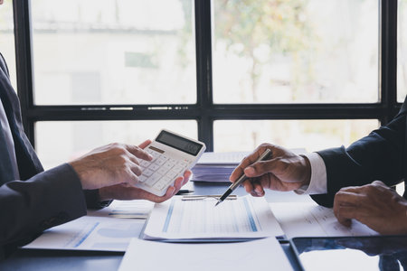 Two Businessman Calculating Bills Using Calculator At Workplace. Business team meeting and discussing project plan. Businessmen discussing together in meeting room.の写真素材