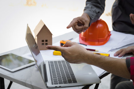 Engineers and architects pointing at laptop screens looking at blueprints. Two Construction Engineers or Architects discussing at work with laptop on construction site and pointing on laptop.の写真素材