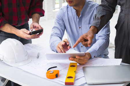 Engineers and architects pointing at digital tablet screens. Two Construction Engineers or Architects discussing at work with digital tablet, laptop and blueprint on construction site.の写真素材