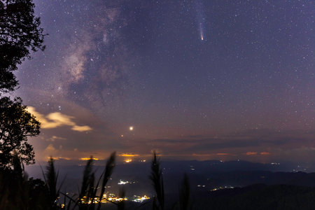 A breathtaking night sky featuring comet C/2023 A3 (Tsuchinshan-ATLAS), the Milky Way, and Venus shining above a tranquil landscape. Perfect celestial view for stargazers and astrophotographers.の写真素材