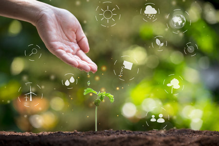 Farmer's hand watering young seedling on fertile soil. Hand nurturing a young plant with digital eco-friendly icons. Concept of sustainable growth, environmental protection, and green technology.の写真素材
