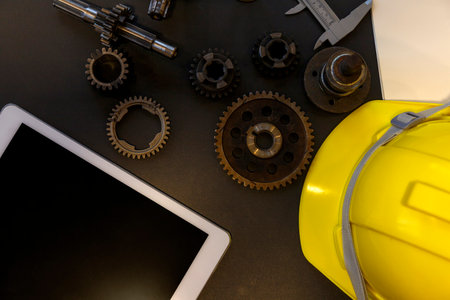 Top view of Gear with machine part, yellow hard hat and a digital tablet with a blank screen on engineer desk.の写真素材