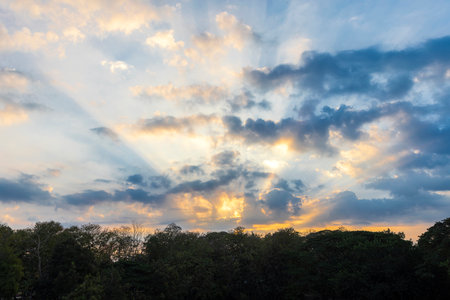 Golden sunlight pierces through scattered clouds, casting a warm glow over the horizon. A breathtaking sunrise paints the sky in hues of orange and blue, blending nature's beauty in perfect harmony.の写真素材