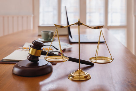 A gavel and scales of justice on a wooden desk symbolize the balance and authority of the legal system. Legal documents and a laptop reflect the modern integration of technology in law.の写真素材