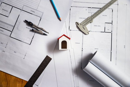 Mini house model on top of architectural blueprints with drafting tools. Real estate planning, architecture, and construction design concept.の写真素材