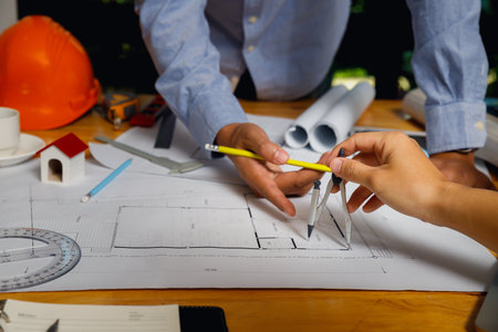 Close-up of engineers collaborating on architectural blueprint with pencil and compass, focusing on...