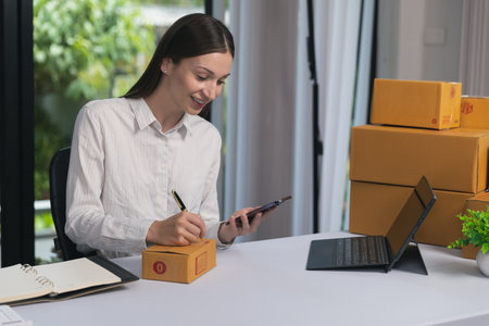 Young businesswoman preparing online delivery packages while using smartphone and laptop at home...