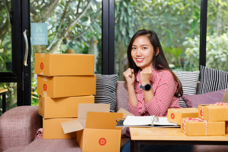 Asian woman celebrating success with parcel boxes at home, concept of online shopping, e-commerce,...