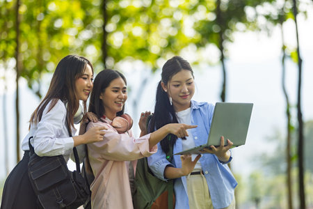 Group of Asian college students standing on green grass and discussing with laptop and books....
