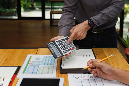 Close-up of two people working on financial planning using a calculator, documents, and reports at a...