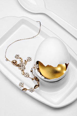 golden jewelry inside broken egg on white egg cup