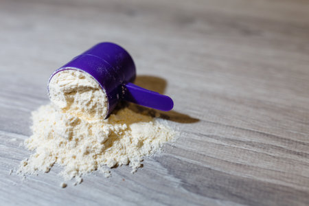 Product photograph of spoon or measuring scoop of whey protein on grey wooden background. Dry mixture for dilution with milk or water.の写真素材