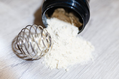 Slide from whey protein, casein or skim milk, spring for the mixture near a black shaker. Fitness and bodybuilding diet for muscle growth. Grey wooden background.の写真素材