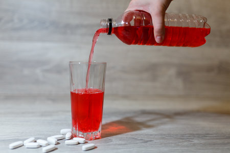 A woman's hand pours a red sports drink or lemonade into a glass Cup from a plastic bottle.の写真素材