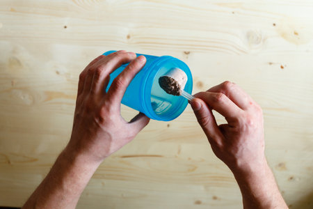 A man pours whey protein shakes to blue. Whey protein, a healthy lifestyle, a person pours whey powder on a bun. And scoop dry mix in man's handsの写真素材