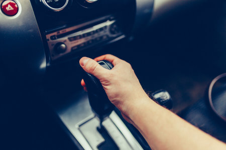 Man's hand switches automatic transmission closeup. Close up view of gear lever manual transmission car interior parts.の写真素材