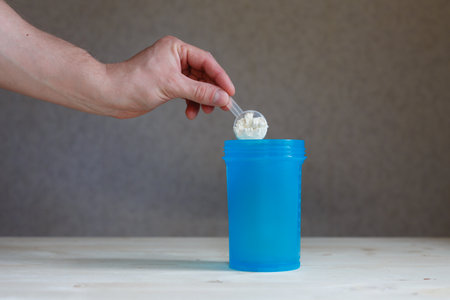 A man's hand holds a scoop of whey protein and pours it into a shaker.の写真素材