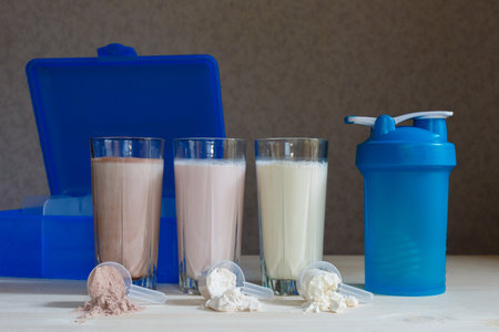 Three milk whey protein shakes in glass cups are arranged in a row with three scoops of protein,...