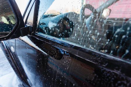 Soapy water drains from the car. A man washes a hand car wash with water under pressure in a car wash outside in a hangar for a car wash.の写真素材