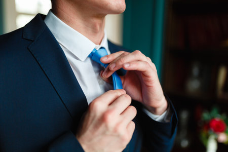 Man in a classic suit straightens his blue tie. Handsome elegant young fashion man in coat tuxedo classical costume suit and bow tie. Portrait of businessman adjusting his necktie standing in officeの写真素材