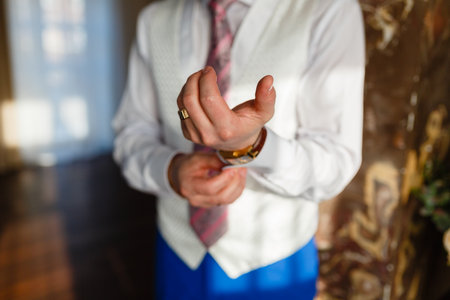 The man fixes the cuffs on the white shirt and stylish vest and blue pants with expensive gold...