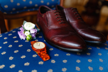 A men's set of accessories on an old wooden chair with a soft seat. The concept of business accessories in clothes. Stylish wristwatch, wooden watch. Men's classic leather shoes, flower boutonniere.の写真素材
