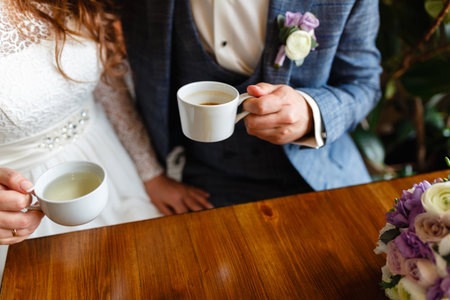 Young couple in a cafe in the attic drinking coffee and tea, sitting. Morning breakfast at the hotel. Cropped image of couple in love holding hands on wooden table while drinking coffee.の写真素材