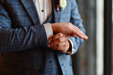 A man in a stylish suit straightens cuffs on his shirt. Shooting of a businessman in a suit. Business concept. Close-up of a man in a tux fixing his cufflink. groom bow tie cufflinks.の写真素材