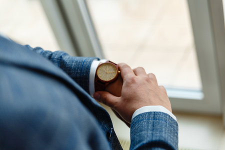 Top view of a man's hands in a suit looking at a wrist watch. Businessman is checking time on his modern wrist watch. Top view. Space for text.の写真素材