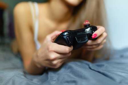 Girl gamer playing with a wireless controller, looking at the screen in front. Young girl eSports player smiling and enjoying the victory with gamepad in hand, playing video games on the console.の写真素材