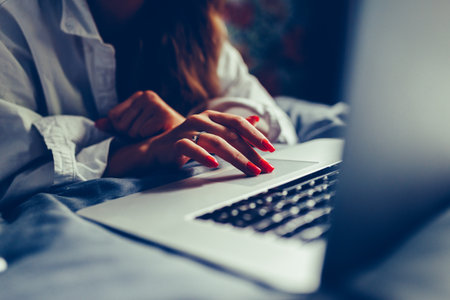 Young attractive and beautiful european woman 20s lying in bed at home using internet working on computer laptop smiling relaxed and cheerful at her bedroom in morning lifestyle concept. Toned photoの写真素材