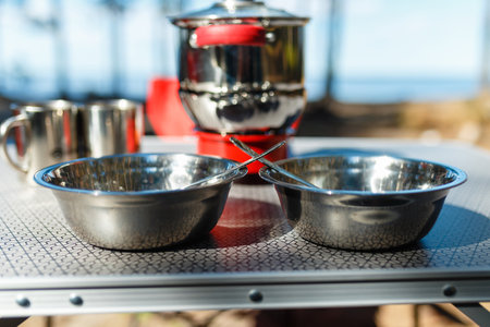 Aluminum pan boil on fire from a portable gas burner next to plates and mugs on a portable table against the background of the red folding chairs in the camping. Cooking while traveling by car.の写真素材