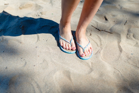 Feet Girl with a neat pedicure in women's stylish beach flip-flops aqua on the beach background. Two sandals on the sand near the sea. The concept of a beach holiday.の写真素材