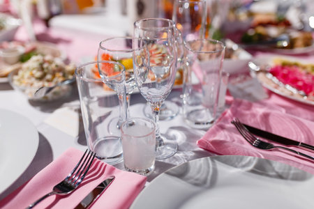 Glasses, forks, knives, napkins and a decorative flower on a white tablecloth table are served for...