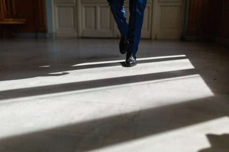 Legs of a man in an expensive suit and black shoes during a step. A person walks along the corridor of the living room or hotel marble floor under the sunlight. Legs close up. Business conceptの写真素材