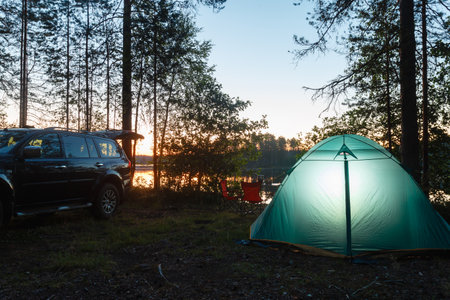 Night landscape with a tent in the forest near lake. The light from the lantern in a tent. Camping in the wild nature.の写真素材