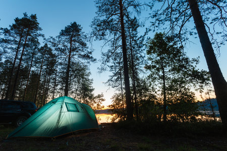 Night landscape with a tent in the forest near lake. The light from the lantern in a tent. Camping in the wild nature.の写真素材