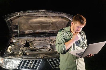A professional car mechanic standing with his back to the car, working in a car service, using a...