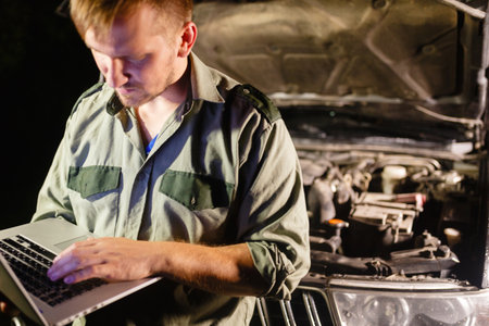 A professional car mechanic standing with his back to the car, working in a car service, using a laptop to set up and check maintenance.の写真素材
