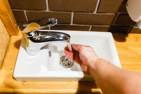 Closeup of male hand turns on the water faucet in the bathroom. Hand open faucet of basin with flow waterの写真素材
