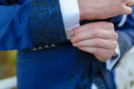 Businessman in a stylish blue suit with patterns adjusts the cuffs of his shirt. Stylish man in an...