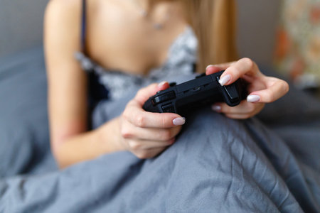 Girl gamer playing video game with wireless joystick at home. Gamepad in female hands close-up,...