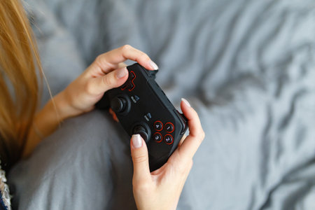 Girl gamer playing video game with wireless joystick at home. Gamepad in female hands close-up,...