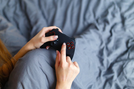 Girl gamer playing video game with wireless joystick at home. Gamepad in female hands close-up,...