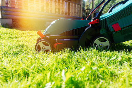 Green electric lawn mower on a freshly mown lawn in the garden against the background of a village house with flare lightの写真素材