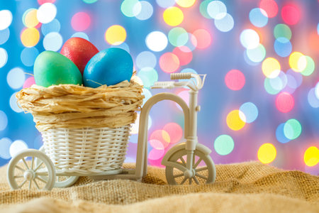Easter card, colored eggs in the nest. Toy Bicycle with a cart. happy Easter. Blue bokeh background. Toy Bicycle with a cartの写真素材